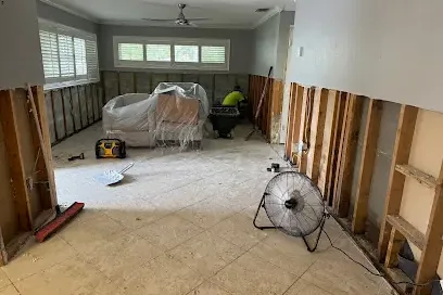 Walls flood-cut above the floor while a fan dries a gutted living room